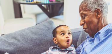 A little boy talking up at his grandfather on the couch