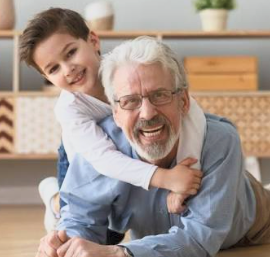 A grandson hugging his laughing grandfather from behind