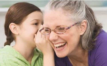 A girl whispering into her grandmother's ear while they both laugh
