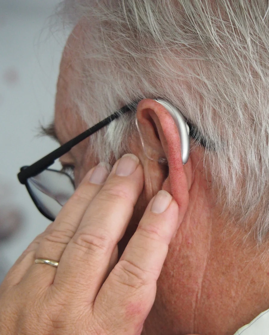 A behind-the-ear hearing aid on an older man's ear